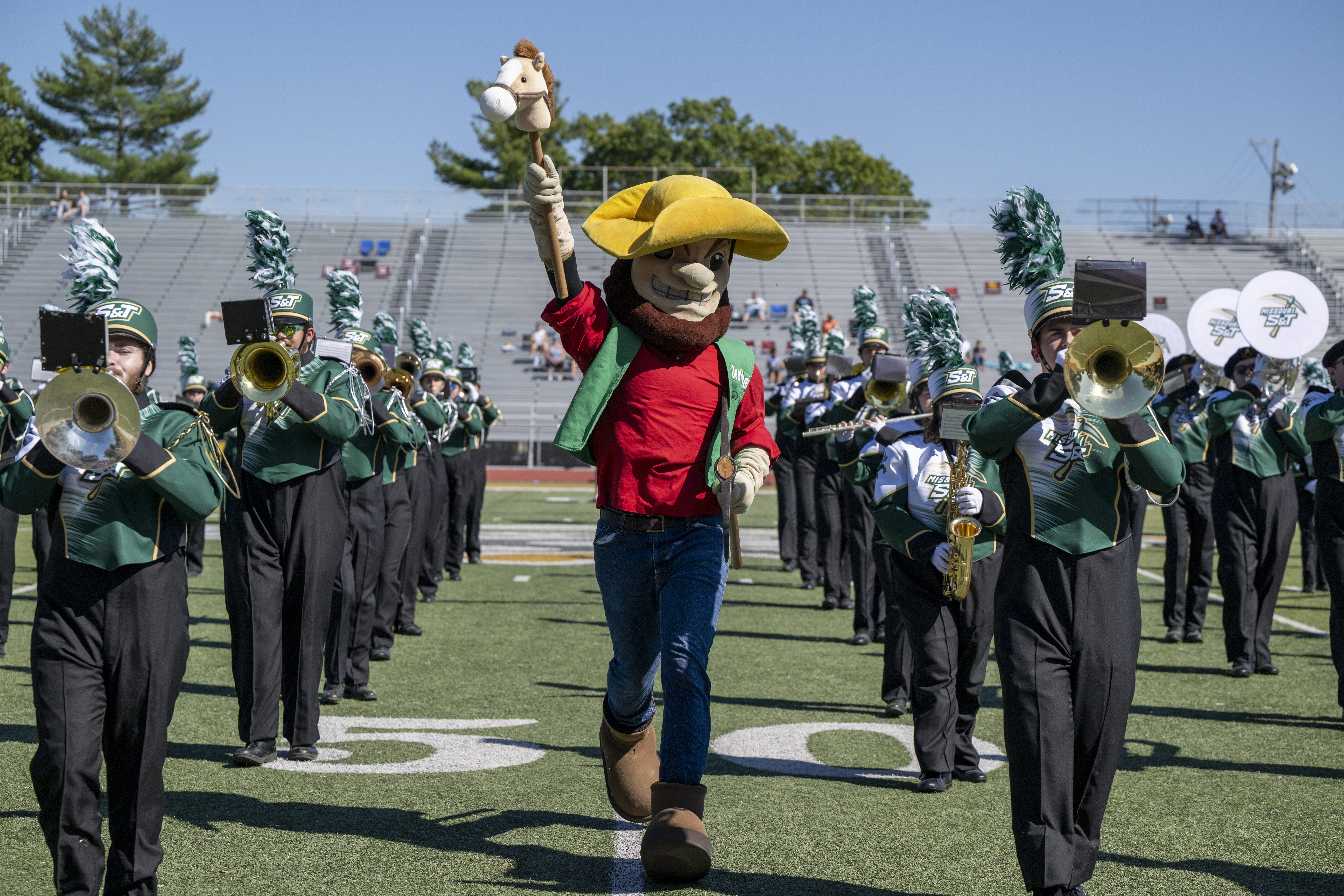 Joe miner leading a marching band. The band wears green uniforms and plays brass instruments